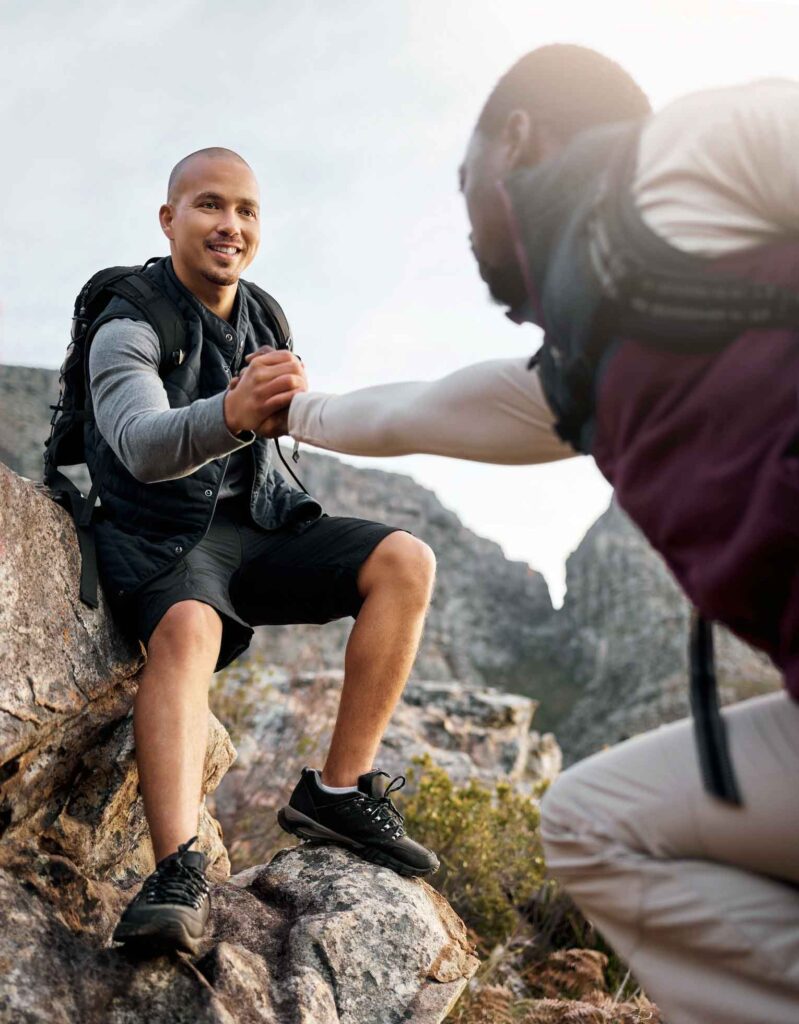 Photo of two men in sober living helping each other up a mountain